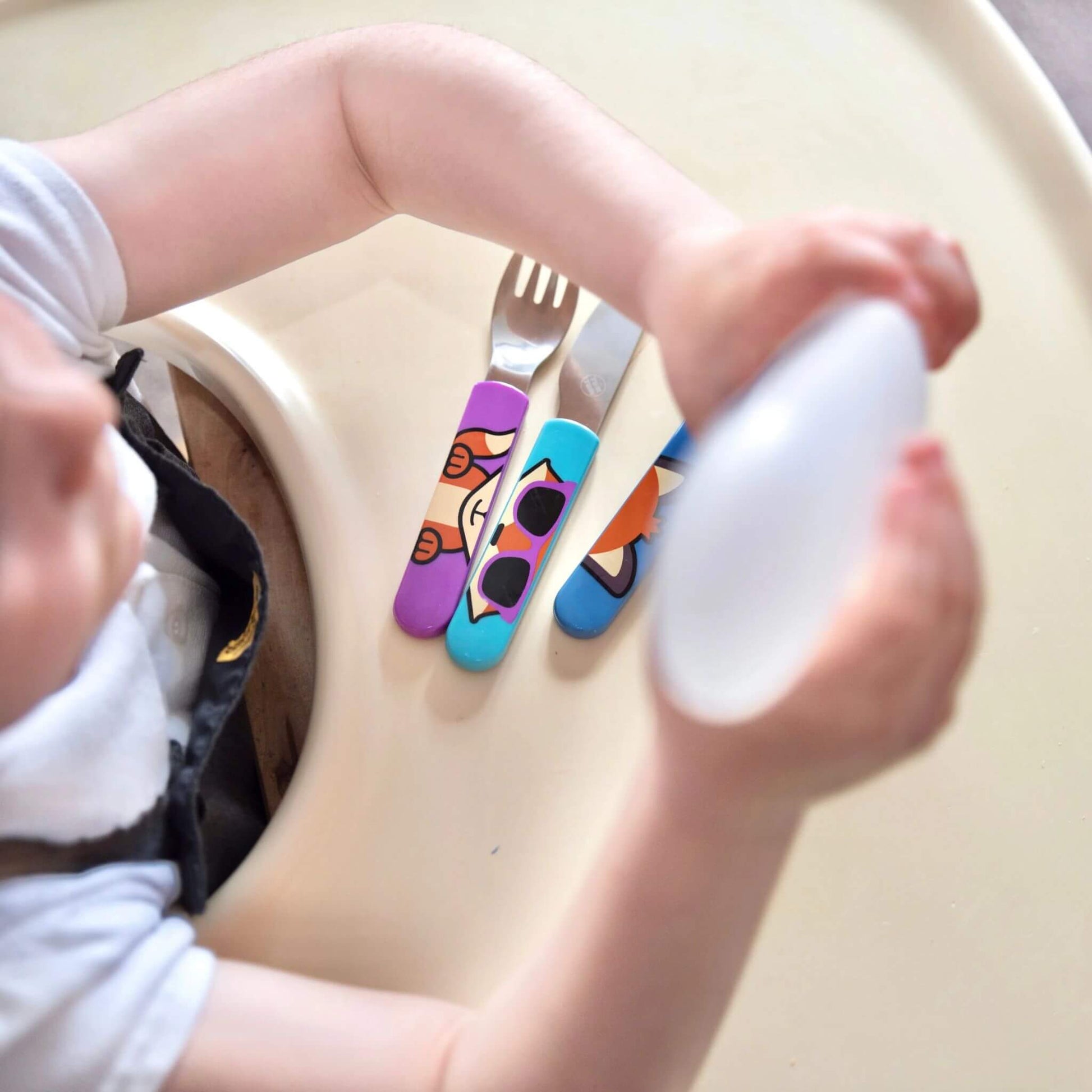 A child seated at a high chair with the TUM TUM Easy Scoop Cutlery Set, featuring colourful Felicity Fox handles on the fork, knife, and spoon. Designed for easy self-feeding.