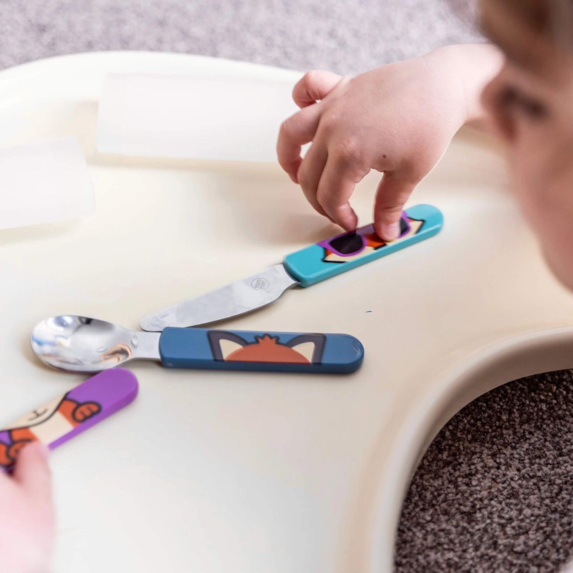 A child playing with the TUM TUM Easy Scoop Cutlery Set, featuring Felicity Fox handles on the spoon, fork, and knife. Designed for easy grip and self-feeding.