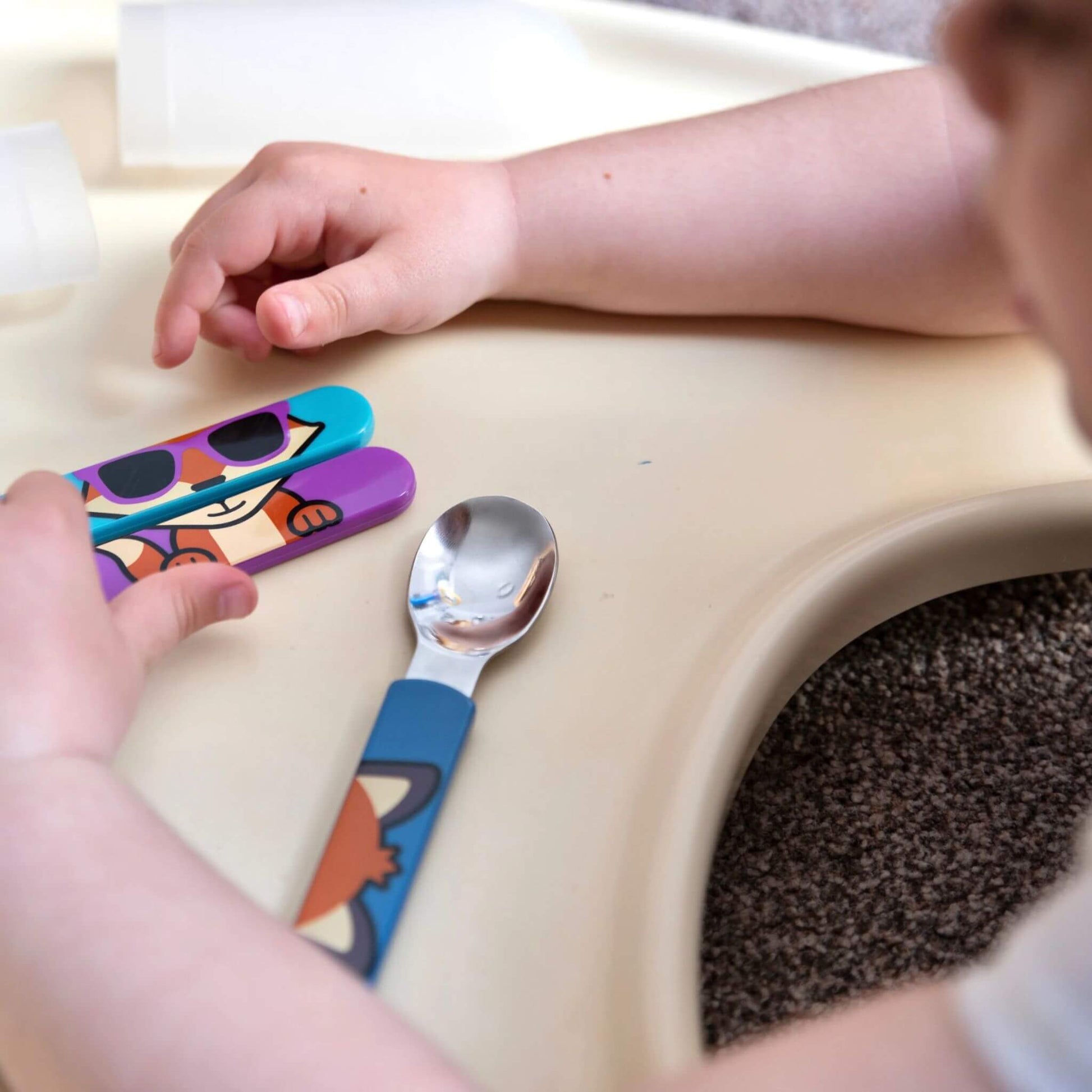 A child interacting with the TUM TUM Easy Scoop Cutlery Set, which includes a spoon, knife, and fork with vibrant Felicity Fox handles. Designed for a comfortable grip and to encourage self-feeding.