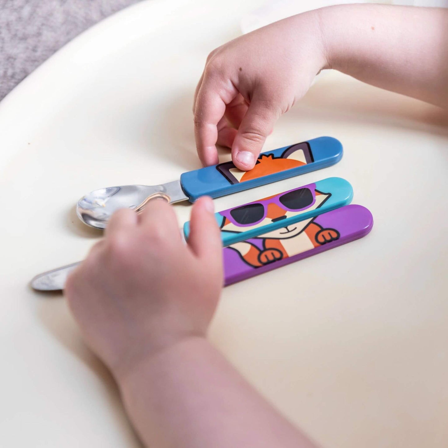 A child arranging the TUM TUM Easy Scoop Cutlery Set, featuring colourful Felicity Fox handles on the spoon, knife, and fork. Designed for easy self-feeding and creativity.