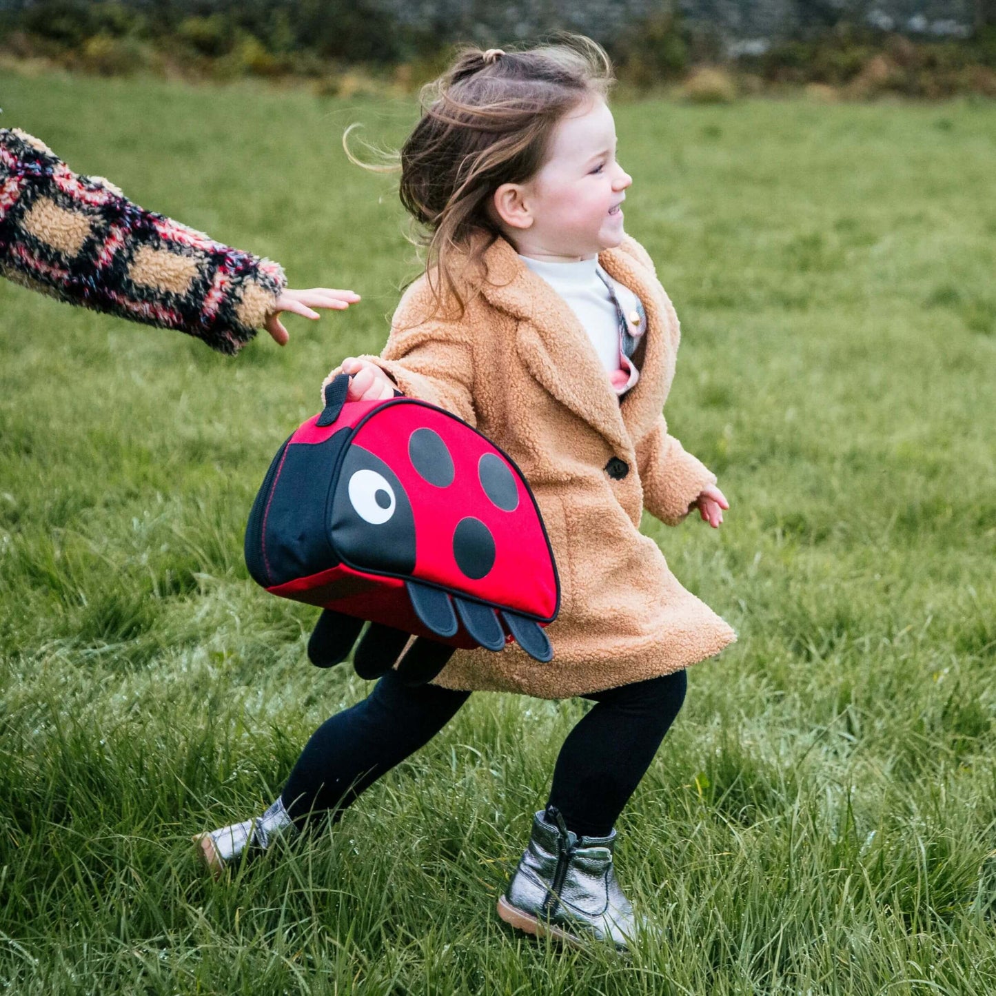 A child running while holding the Ladybird TUM TUM insulated lunch bag, perfect for active play, school lunches, and outdoor adventures.