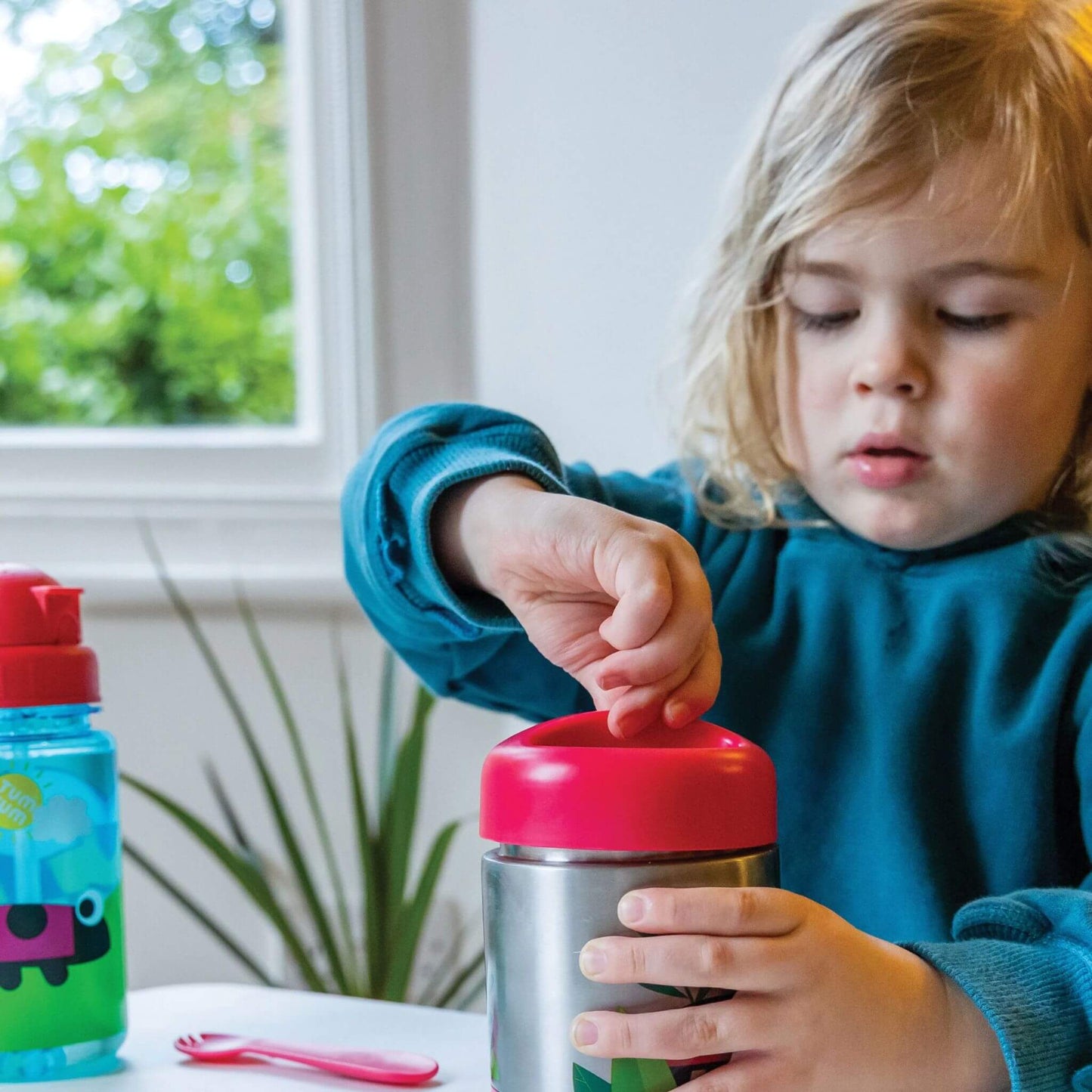 Child opening an insulated food flask with red lid, perfect for keeping food hot or cold, with easy-to-use design for little hands.