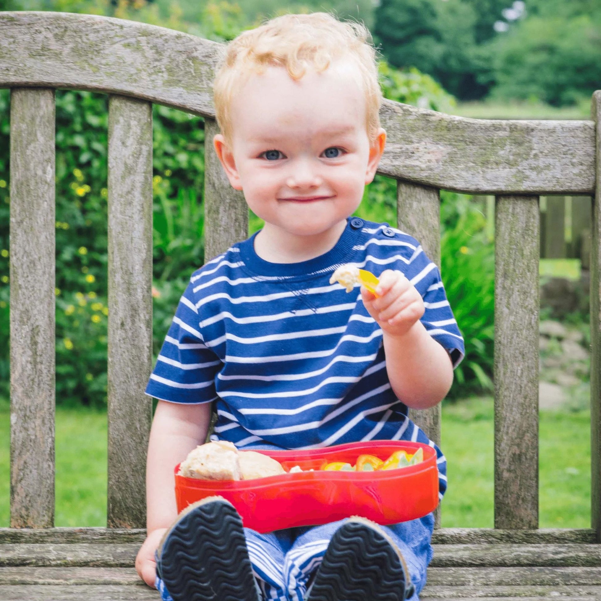 Young child enjoying a meal outdoors with the TUM TUM Lunch Box with Dipping Pot Separator, perfect for healthy snacks on the go.