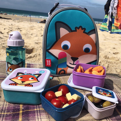 TUM TUM Felicity Fox Nesting Snack Pots, water bottle, and lunch bag on a beach, filled with snacks like tomatoes, cheese, and peaches.