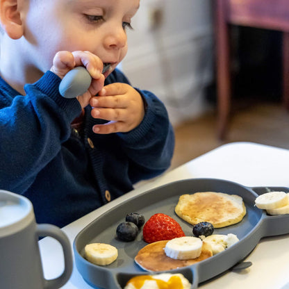 Toddler using TUM TUM silicone cutlery set, enjoying pancakes and fruit on a toddler-friendly plate, perfect for self-feeding.