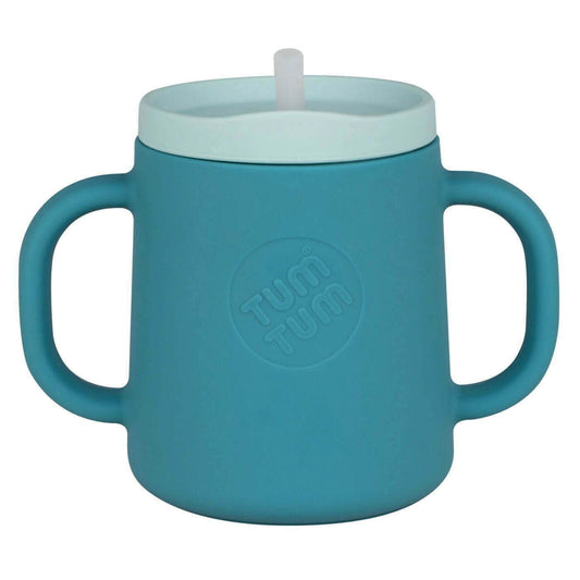 A blue TUM TUM silicone sippy cup featuring dual handles for easy gripping. The cup includes inner measurement markings for tracking liquid intake, making it ideal for toddlers learning to drink independently.