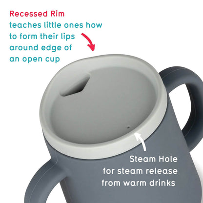 A grey TUM TUM silicone sippy cup with a recessed rim designed to help toddlers learn to form their lips around the edge of an open cup. It features a steam hole for safe steam release from warm drinks, ensuring comfort and safety during use.