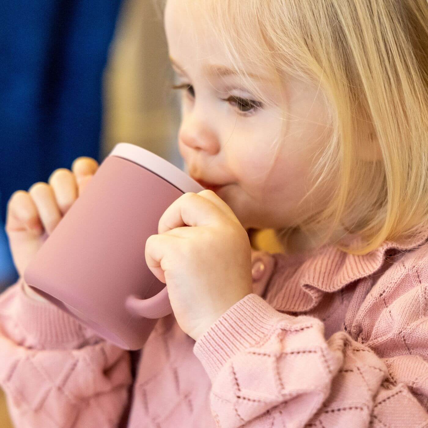 A toddler is drinking from a pink TUM TUM silicone sippy cup with dual handles, designed for easy gripping. 