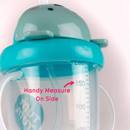 A close-up of the TUM TUM Tippy Up Cu, featuring a blue bear lid and dual handles. The cup shows a handy measurement scale on the side for easy tracking of fluid intake. The weighted straw inside follows the liquid for smooth, any-angle drinking.