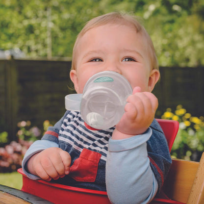 A baby happily drinking from a TUM TUM Tippy Up Cup. The cup has clear handles and a weighted straw that follows the liquid, allowing the baby to drink comfortably from any angle. Ideal for toddlers learning to drink independently.