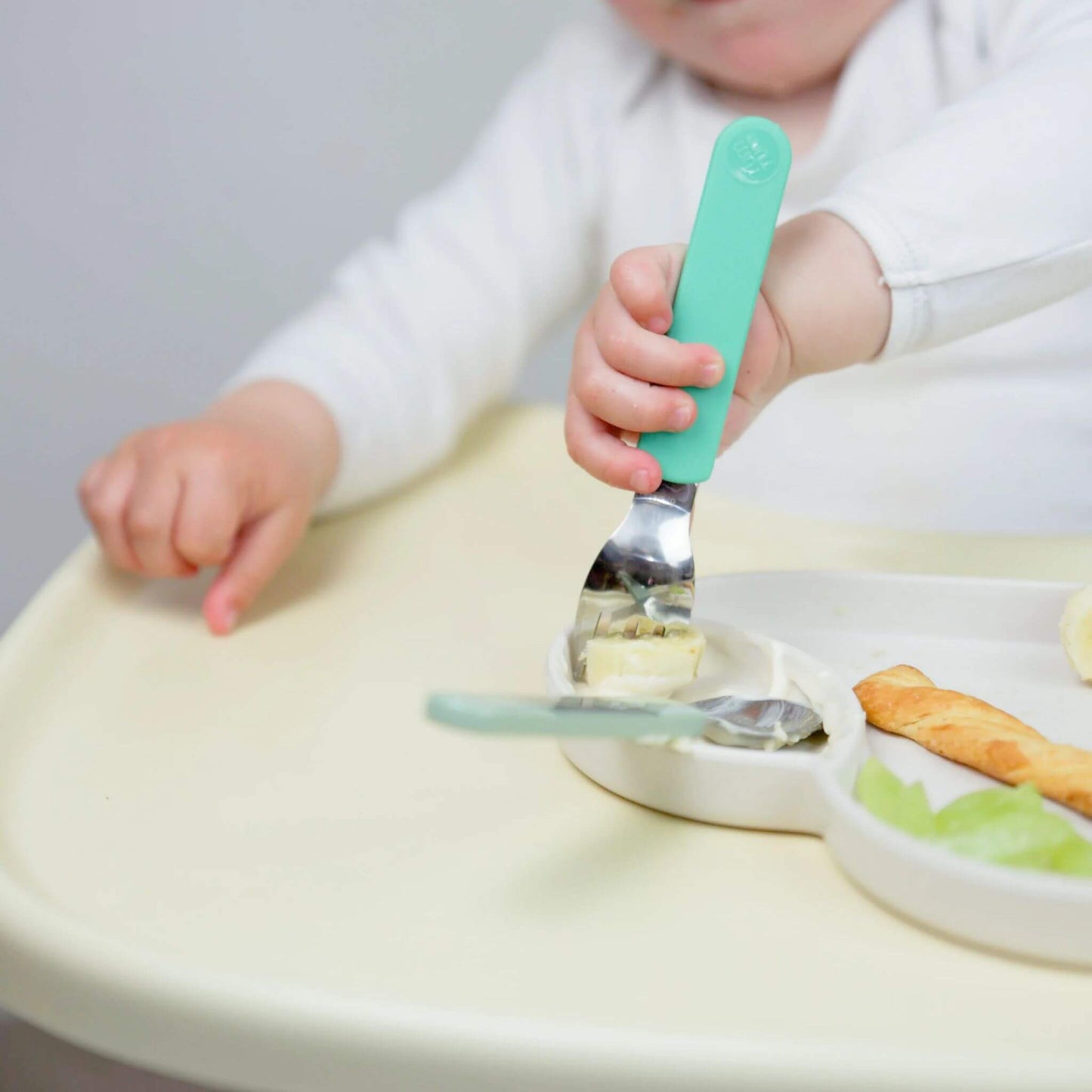 A child using the TUM TUM Easy Scoop Cutlery Set to eat, holding the fork with a comfortable grip. Designed for self-feeding, featuring Stanley Sloth handles.