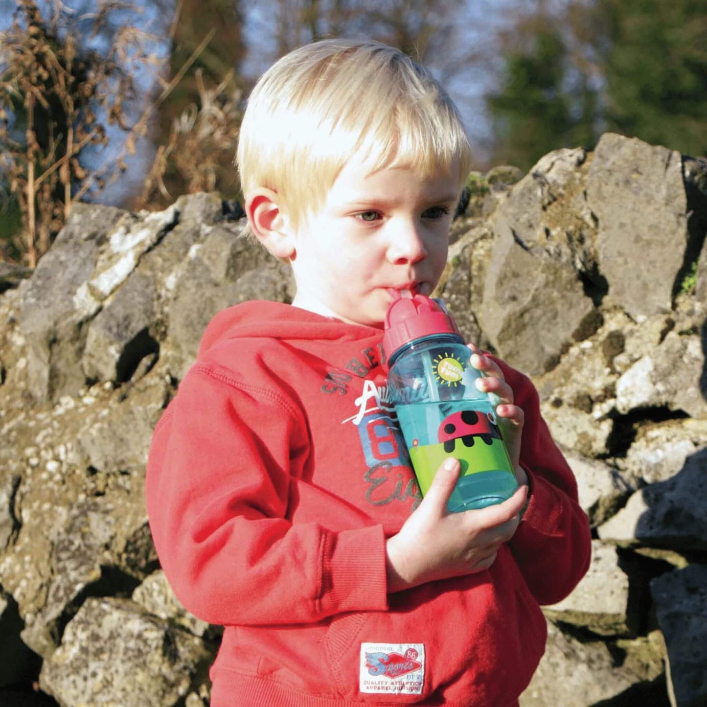 Child drinking from TUM TUM water bottle with bugs design, featuring a flip top lid and straw, perfect for keeping kids hydrated.