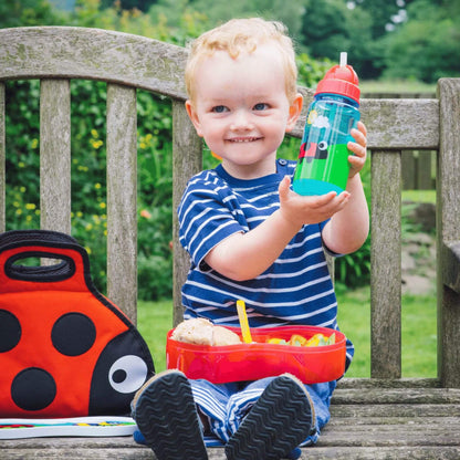 Smiling child holding TUM TUM water bottle, sitting with matching lunchbox and bag, perfect for kids on the go.