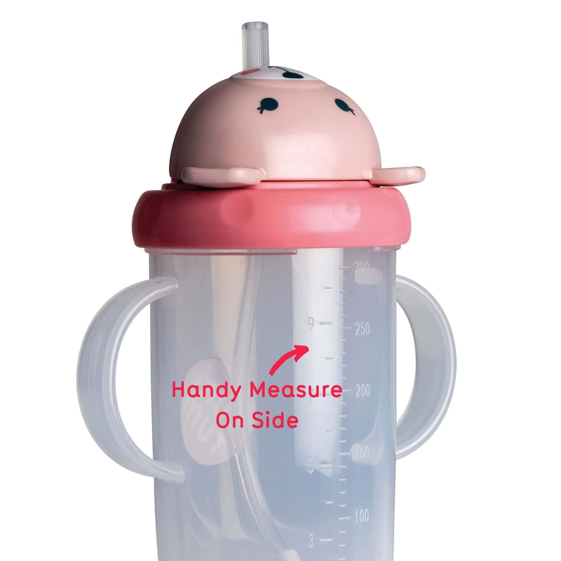 A clear sippy cup with dual handles, featuring a pink bear lid and a built-in straw. The cup has a flip-top lid and a measuring scale on the side to track fluid intake, ideal for toddlers.