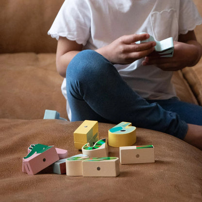 Child playing with Vilac Magnetic Jungle Animals Set wooden blocks on sofa, developing fine motor skills through creative play.