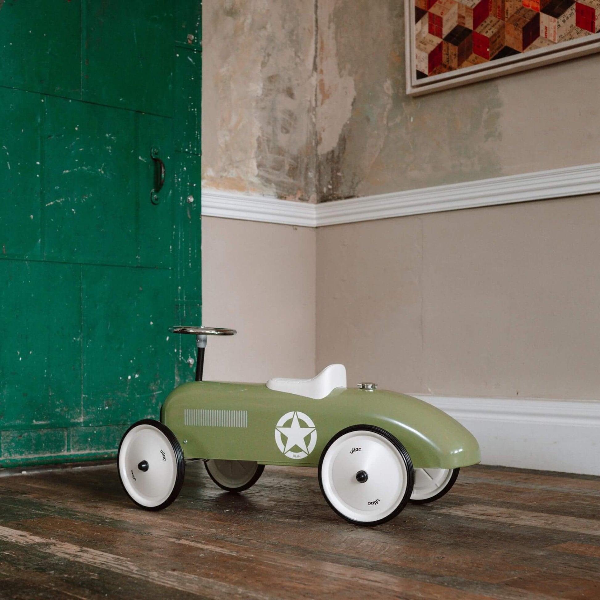 Vilac Classic Metal Car in khaki green with white seat, silver steering wheel, and star emblem, set against a rustic interior backdrop.