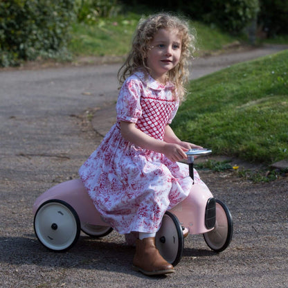 Young girl  riding the Vilac Classic Metal Car in pink with silver steering wheel.