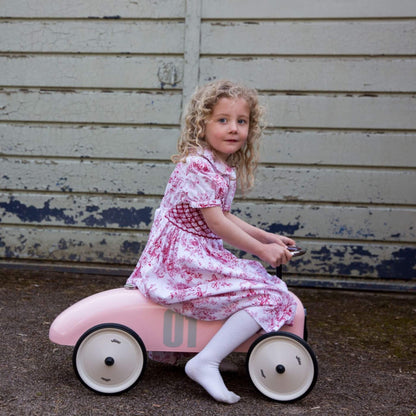 Young girl riding the Vilac Classic Metal Car in pink with number 01 detail on the side.