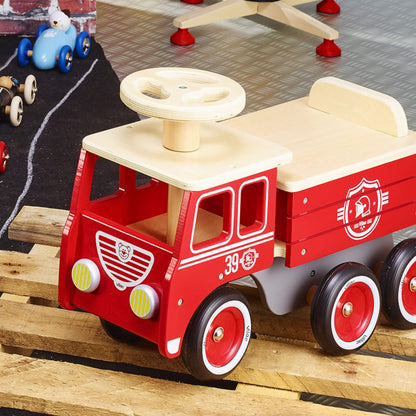 The Vilac Ride-On Fire Truck sits on a wooden pallet, showcasing its classic red design, rubber wheels, and wooden steering wheel.