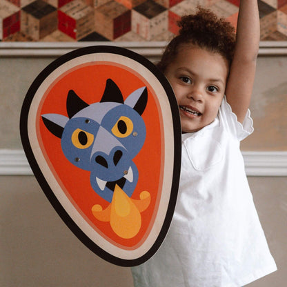 A smiling child proudly holding the Vilac dragon-themed wooden shield, showcasing its bold design of a fire-breathing dragon, perfect for imaginative adventures.