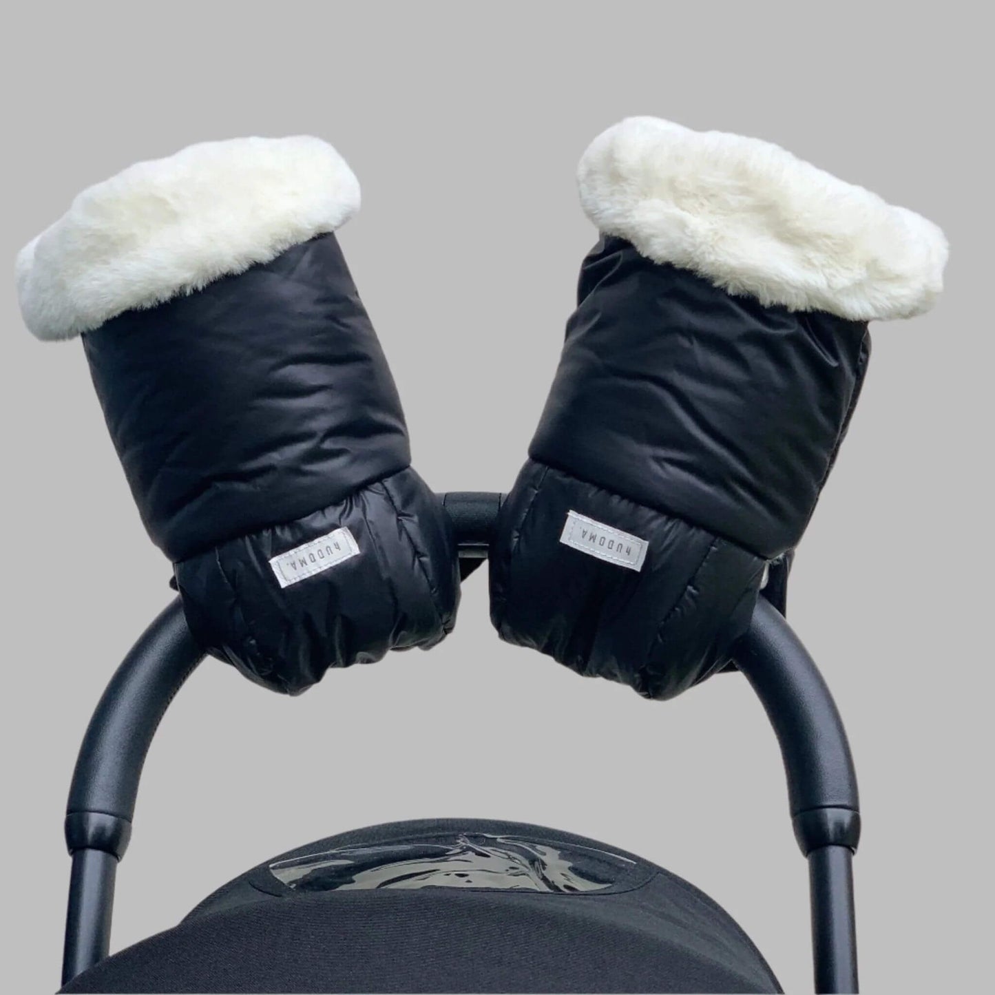 Front-facing view of hUDOMA Chelsea Black Pram Gloves securely attached to a stroller handle, showcasing their black exterior and plush white faux fur lining for ultimate warmth and style during winter walks.