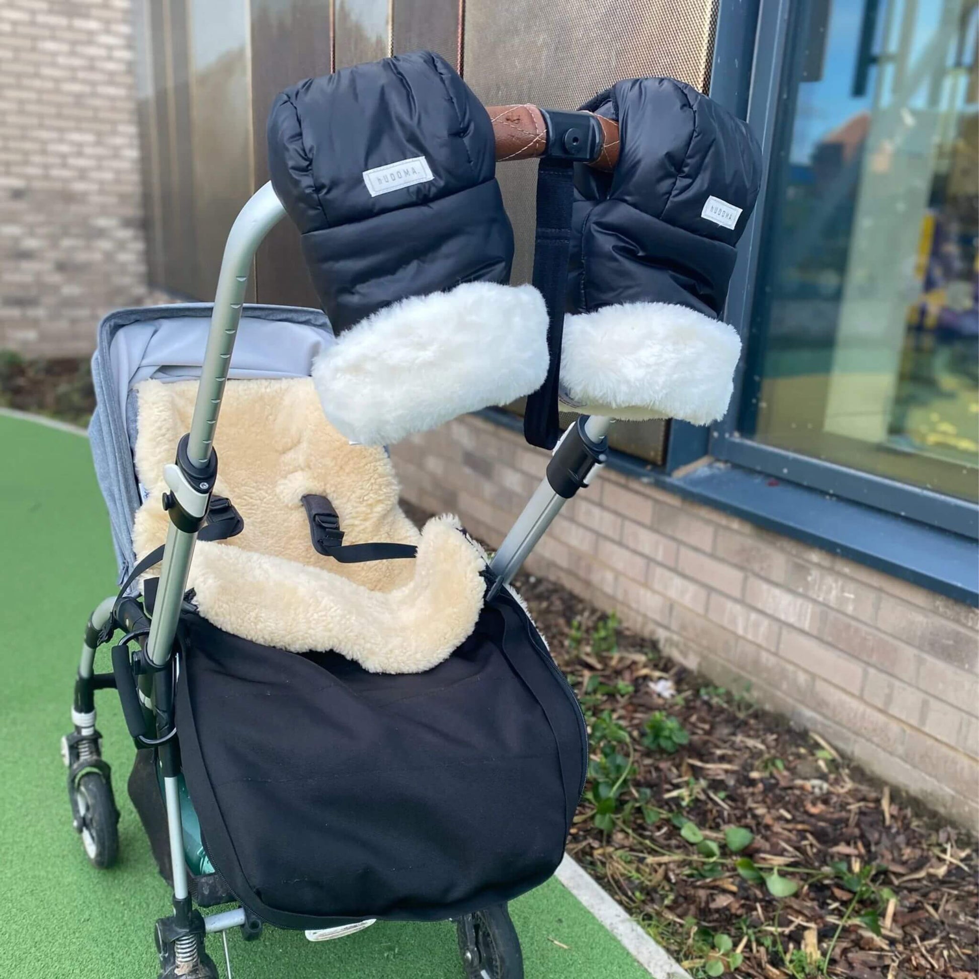 Outdoor lifestyle image of a stroller featuring the hUDOMA Chelsea Black Pram Gloves securely attached to the handle, showcasing their sleek black design with soft white faux fur lining, paired with a cosy sheepskin liner, ideal for cold-weather strolls.